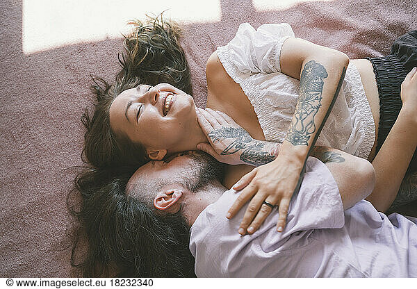 Happy hipster couple with tattoos lying on bed at home
