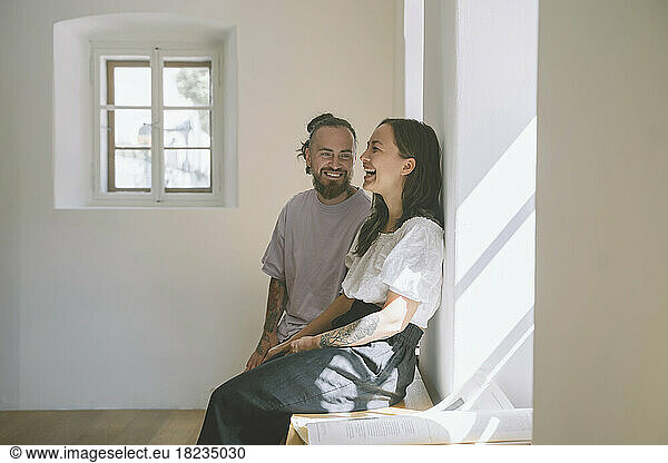 Happy hipster man with girlfriend sitting on table in front of wall at home
