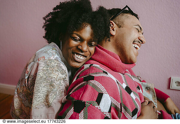 Happy hipster woman embracing gay man at home
