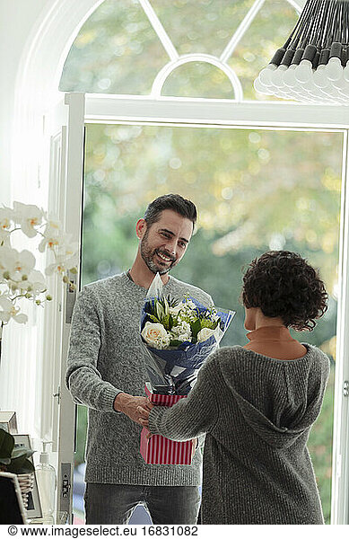 Happy husband surprising wife with flowers at front door