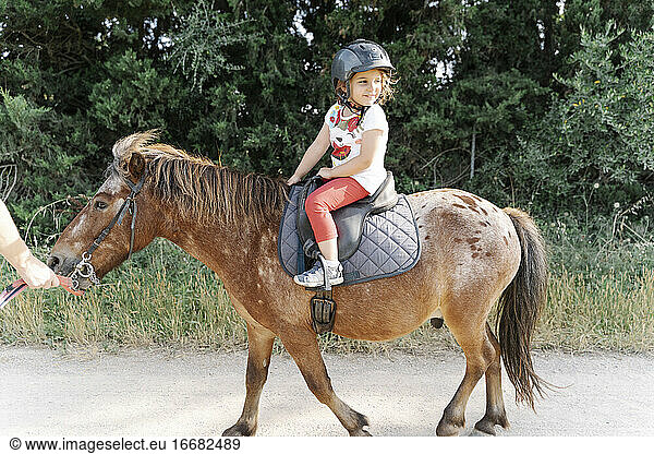 Happy kid riding horse in paddock