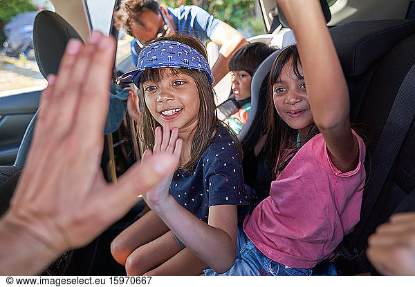 Happy kids high-fiving in back seat of car