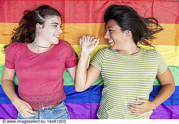 Happy lesbian couple holding hands lying on rainbow colored flag