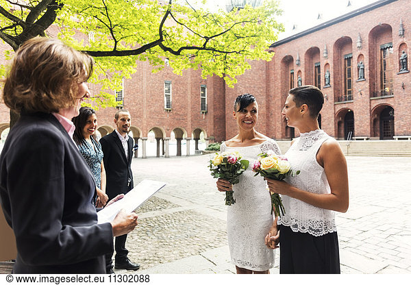 Happy lesbian couple standing in front of female priest for wedding ceremony