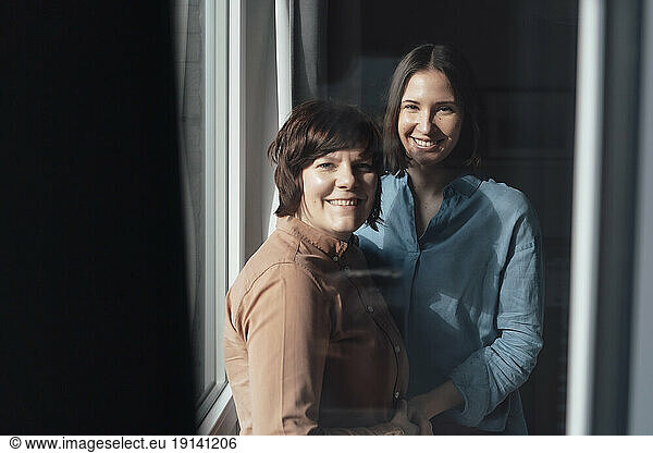 Happy lesbian couple standing near window at home