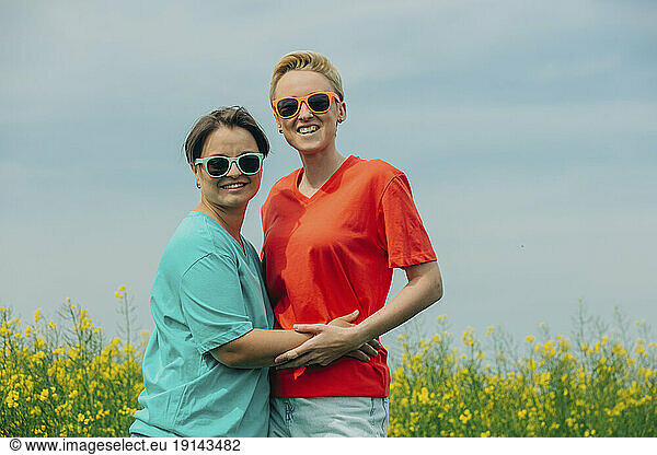 Happy lesbians wearing sunglasses standing at field