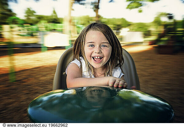 Happy little girl spinning on playground toy