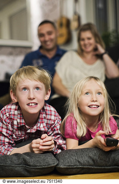 Happy little siblings watching TV with parents sitting behind