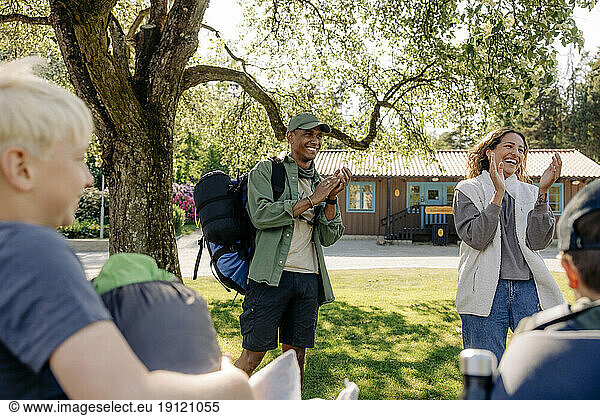 Happy male and female camp counselor clapping while standing with kids at summer camp