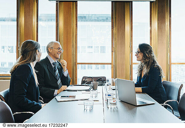 Happy male and female colleagues discussing at conference table in board room