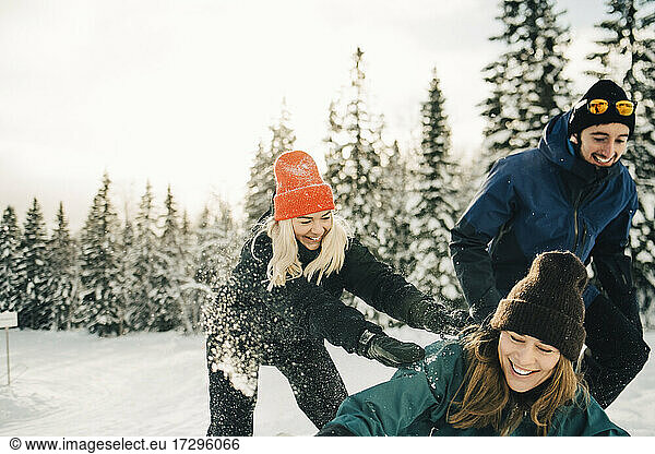 Happy male and female friends playing at ski resort during winter