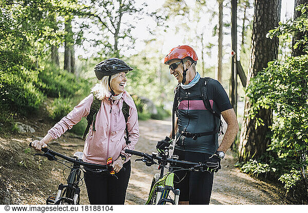 Happy male and female friends talking to each other holding cycles