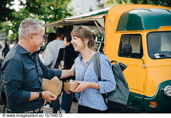 Happy male and female friends talking while standing with food box against commercial land vehicle