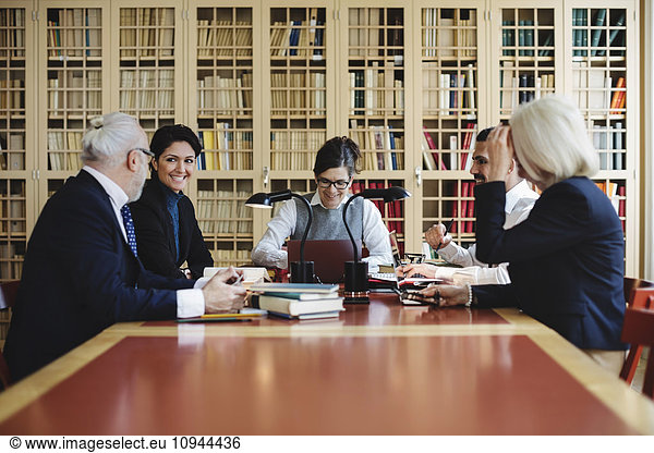 Happy male and female lawyers sitting in board room against bookshelf