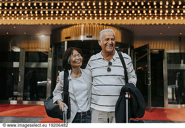 Happy male and female senior friends standing in front of movie theater