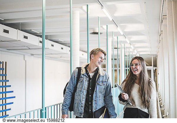 Happy male and female students walking in corridor of university