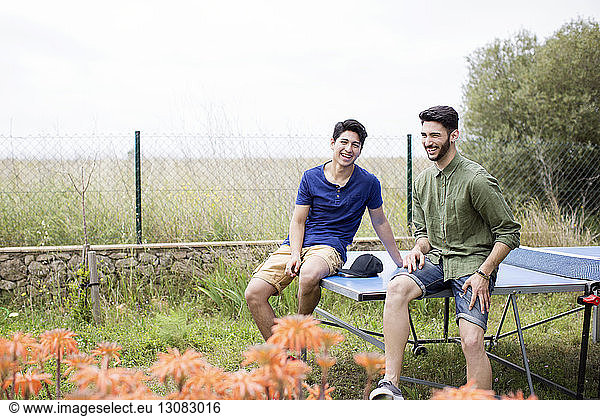 Happy male friends sitting on tennis table at yard
