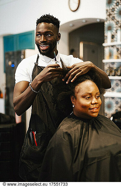 Happy male hairdresser cutting hair of female customer in barber shop