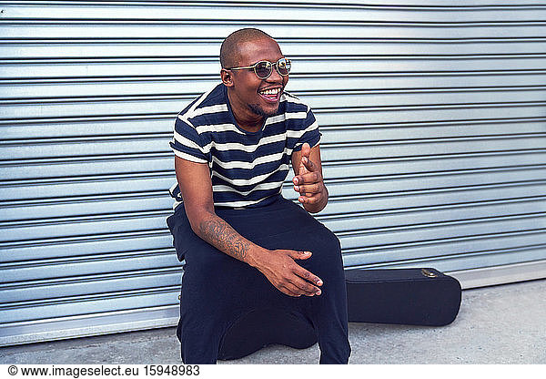 Happy male musician sitting on guitar case outside garage