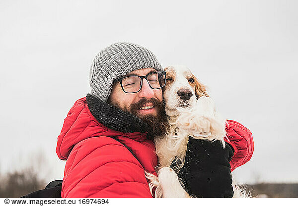 Happy male person hugs his spaniel dog at a walk.