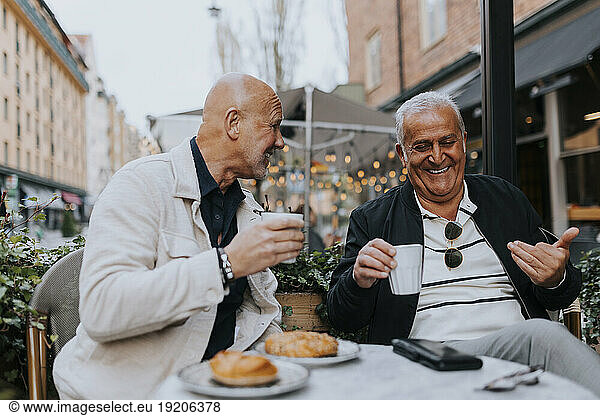 Happy male senior friends enjoying with each other while having coffee at sidewalk cafe