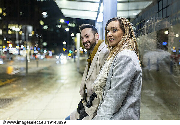 Happy man and woman leaning on glass at footpath