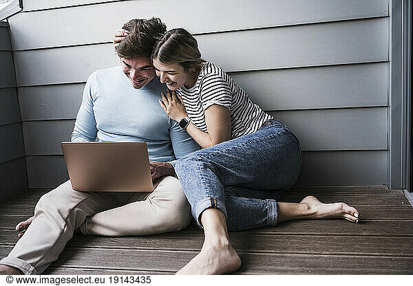 Happy man and woman using laptop in front of wall