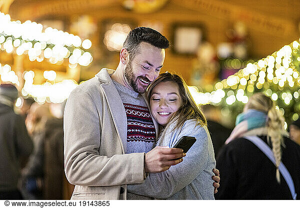 Happy man and woman using mobile phone at Christmas market