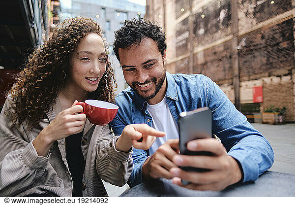 Happy man and woman using smart phone at sidewalk cafe