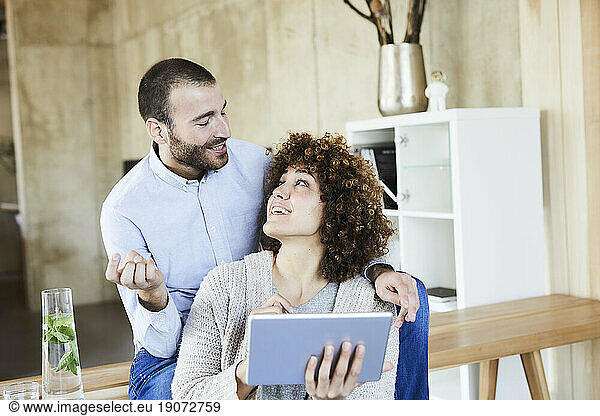 Happy man and woman with tablet talking in modern office