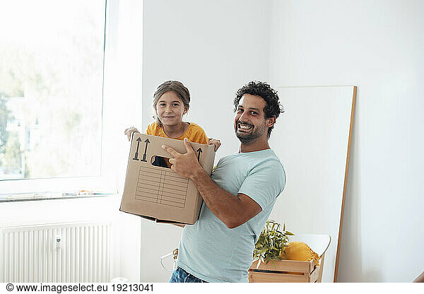 Happy man carrying daughter in cardboard box at home