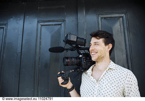 Happy man carrying digital video camera while standing against door