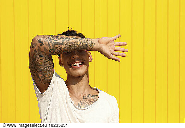 Happy man covering eyes with hand in front of yellow wall