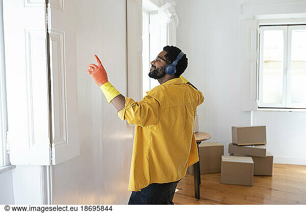 Happy man enjoying music with headphones and cleaning new apartment