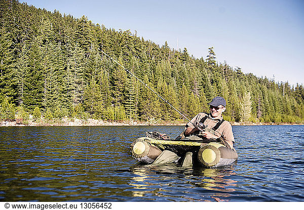 Happy man fishing while sitting on pontoon boat in lake