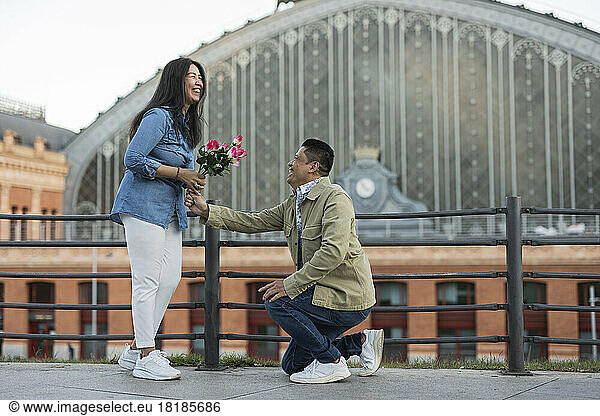 Happy man giving flowers to woman and proposing at footpath on Valentine's day