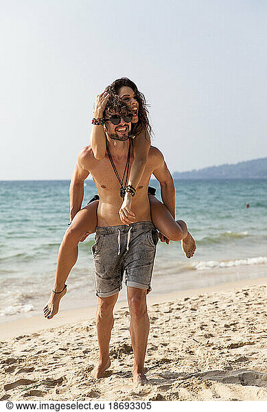 Happy man giving piggyback ride to girlfriend at beach