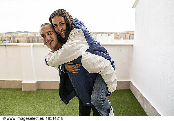 Happy man giving piggyback ride to girlfriend at terrace