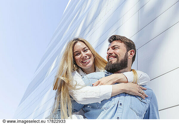 Happy man giving piggyback ride to woman in front of wall