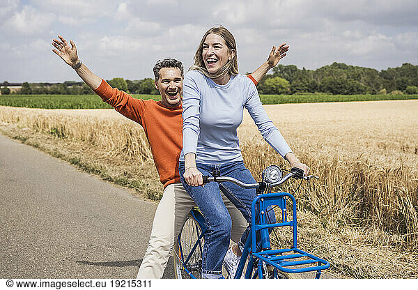 Happy man having fun with woman riding bicycle near field