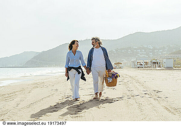 Happy man holding basket and walking with woman at beach