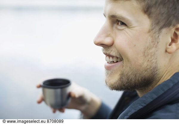 Happy man holding coffee cup against lake