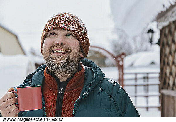 Happy man holding coffee mug looking up in winter