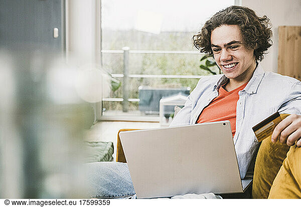 Happy man holding credit card doing online shopping through laptop at home