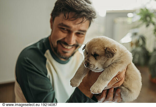 Happy man holding mixed breed puppy at home