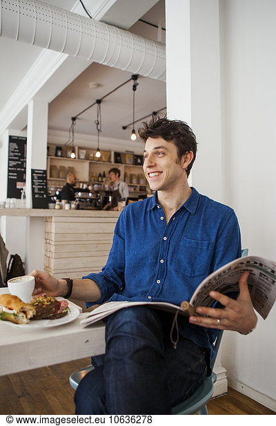 Happy man holding newspaper while having breakfast at cafeteria