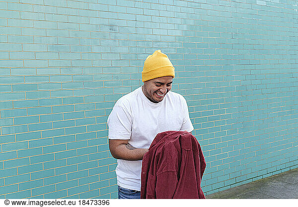 Happy man holding red shirt standing in front of turquoise colored wall