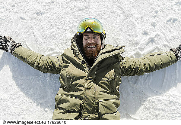 Happy man in warm clothing lying on snow with arms outstretched
