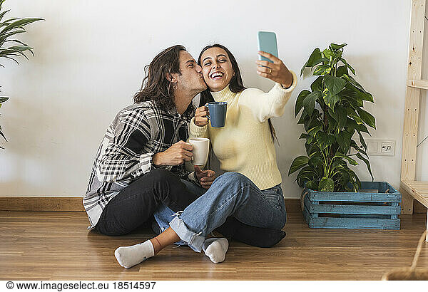 Happy man kissing girlfriend taking selfie at home