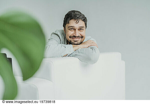 Happy man leaning on sofa in front of white wall